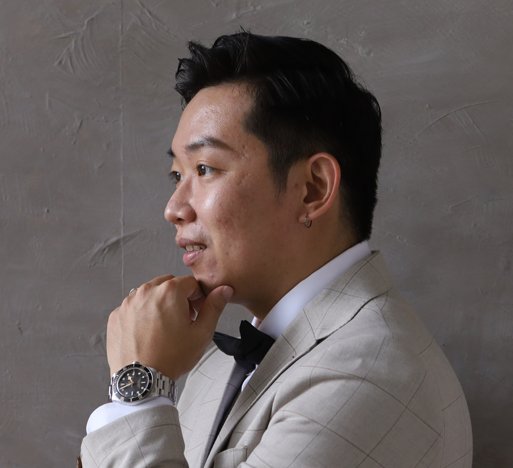 Logan Lam in a light check blazer and bow tie, chin resting on his hand.